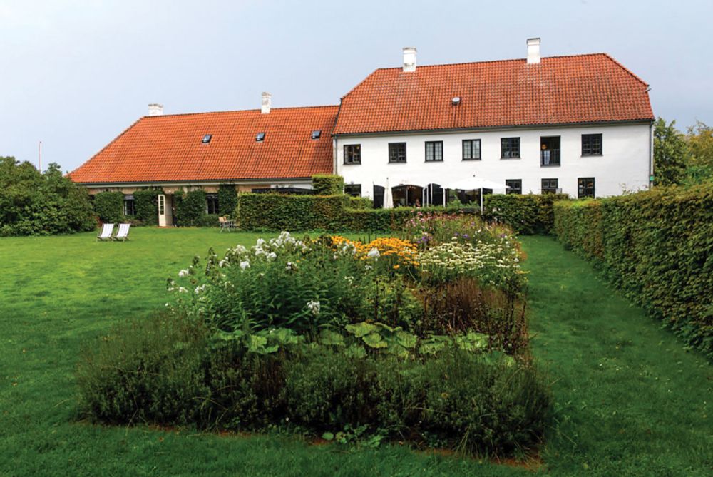 Danish farmhouse with red roof sits in a green field.