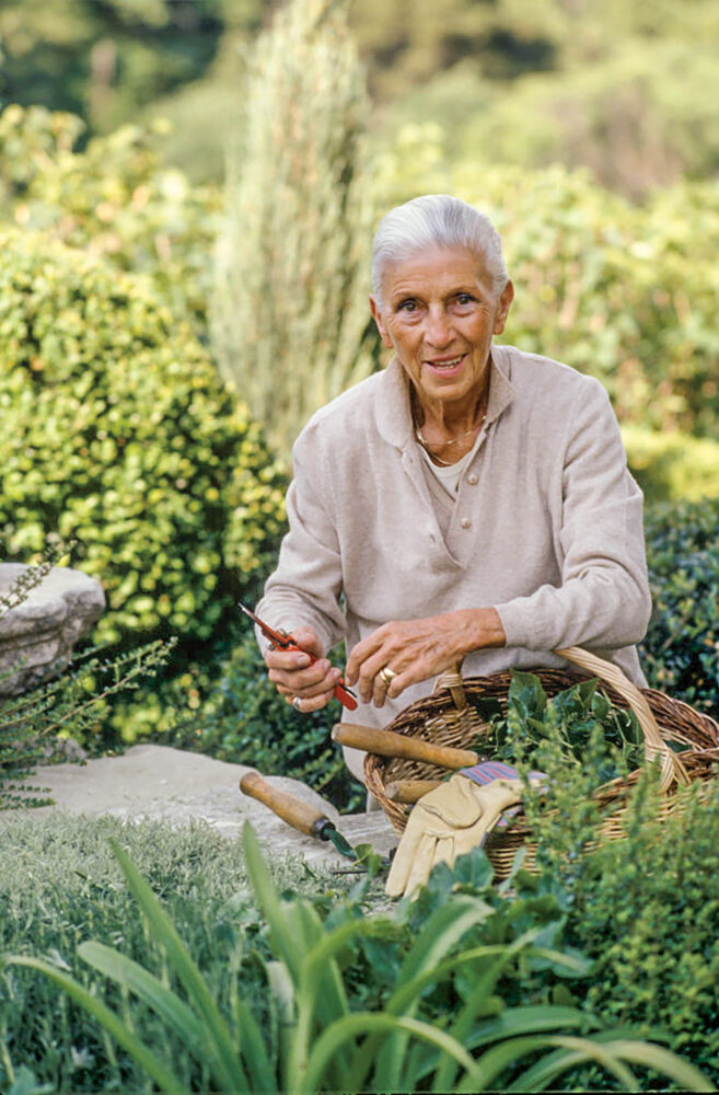 Nicole de Vésian sits in her green garden with her tools.