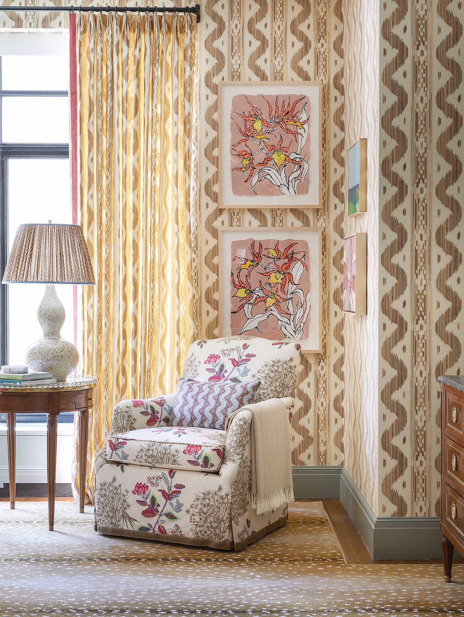 A floral print chair sits in the corner of a striped wallpaper room.