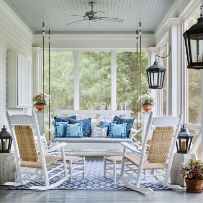 Photo the screened porch at McCurdy Plantation. Designer James Farmer chose a gray floor and light blue ceiling, and furnished it with two rocking chairs and a bed swing covered in blue pillows.
