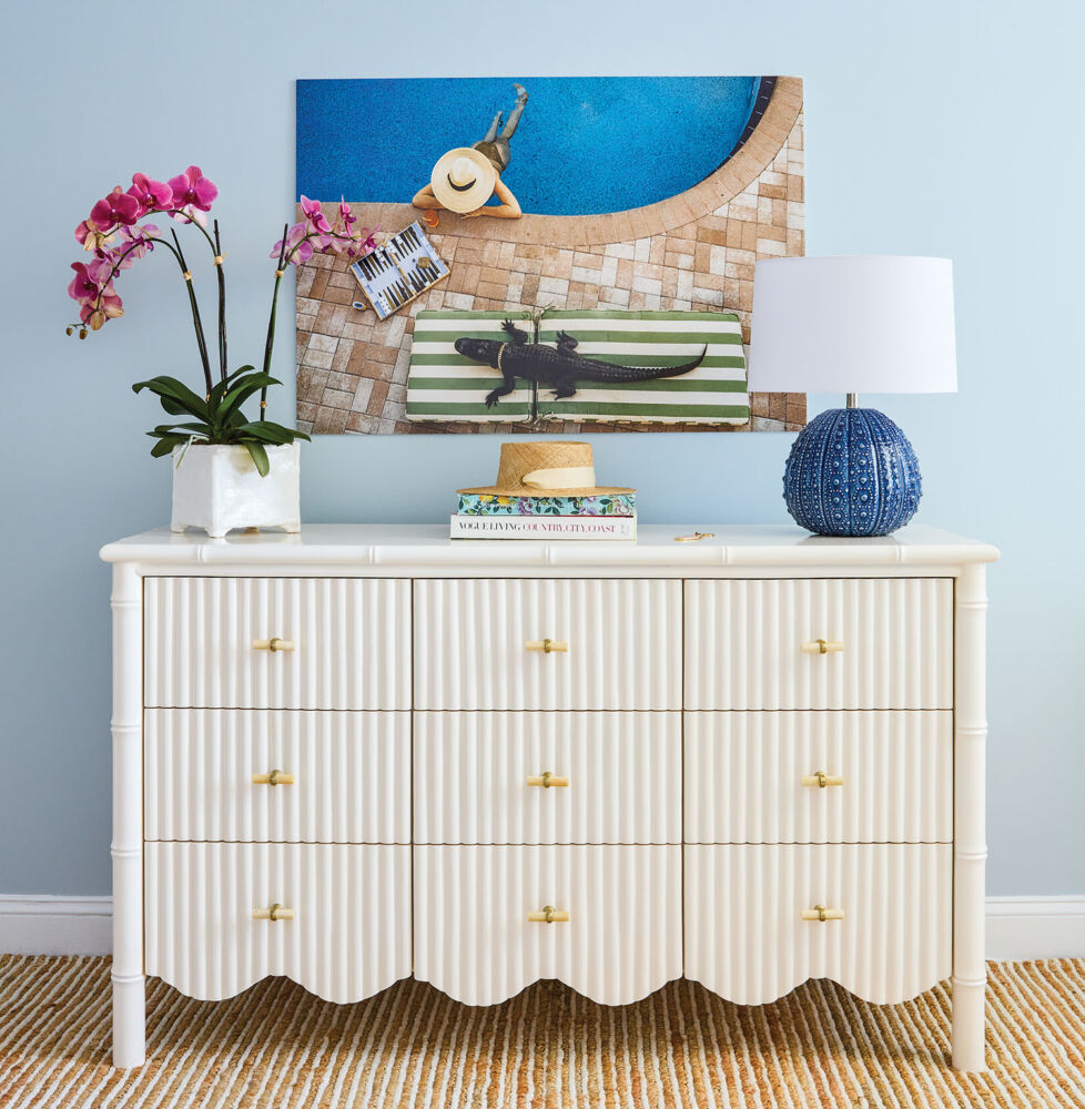 A white dresser with scallops at the front sits in front of a pale blue wall.