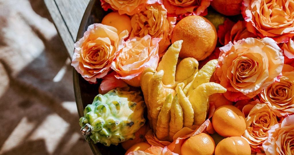 Shallow bowl filled with orange rose blossoms, Buddha's hand citron, and other citrus.