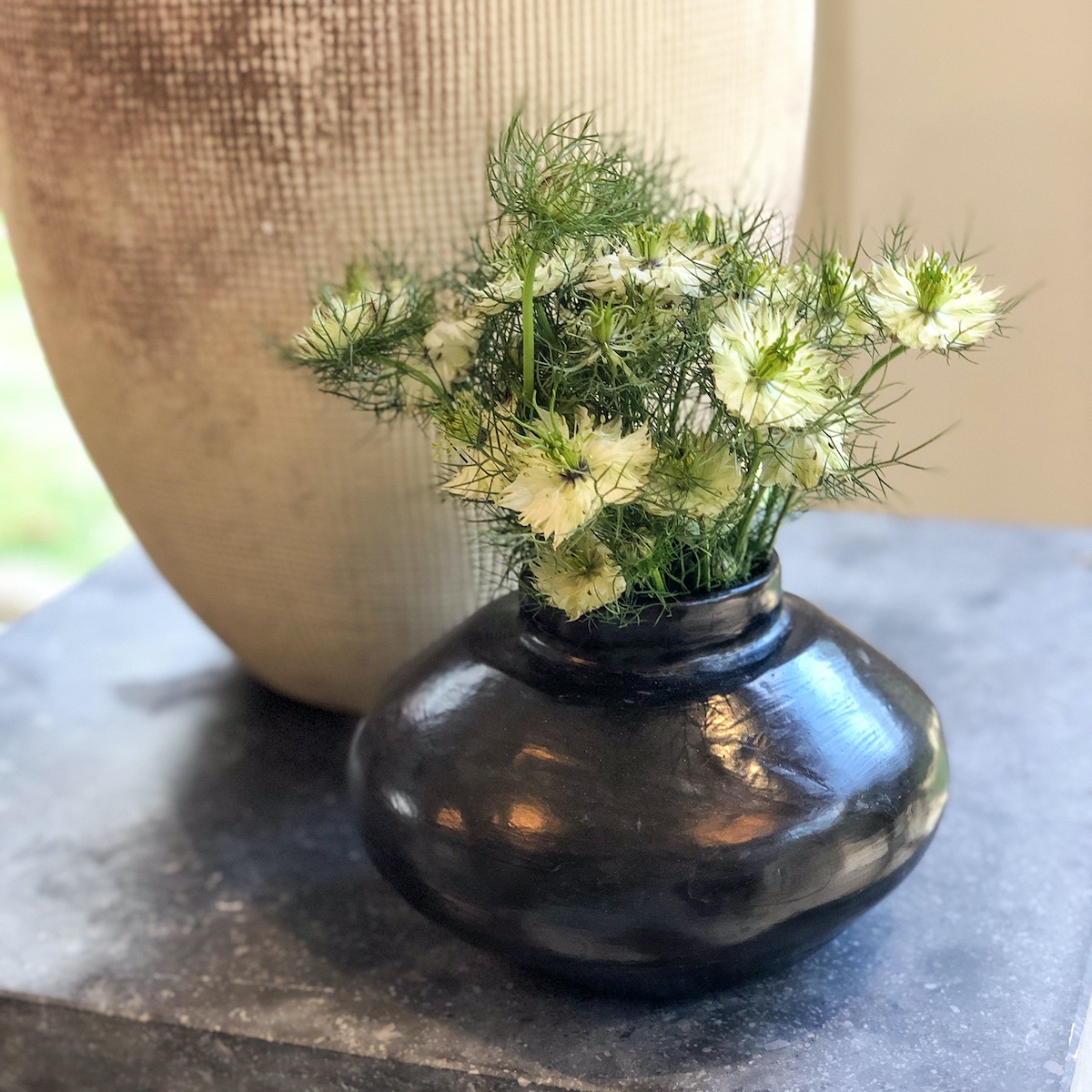 Small black vase filled with greenish white nigella flowers by Keith Robinson. Vase sits on end table in Ashley Whittaker designed screened porch at the Flower Atlanta Showhouse.