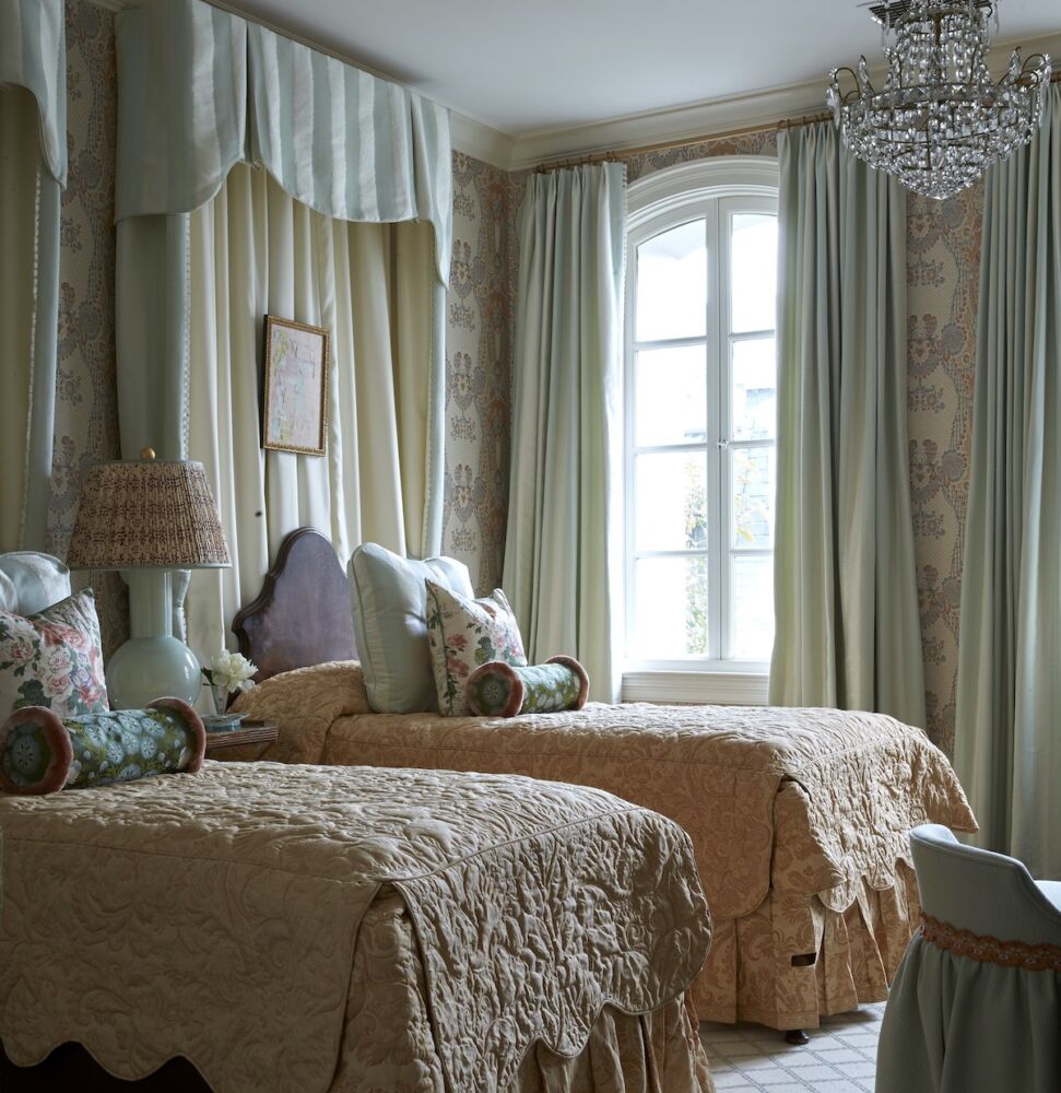 Guest room with two beds with the headboards against ceiling-height pleated drapery and added a crystal chandelier and a bedside reading lamp.
