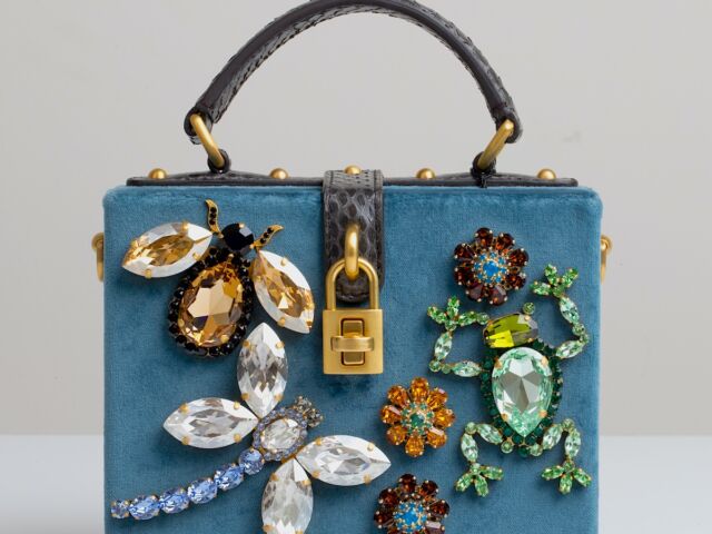 A bejeweled bee, a diamond encrusted dragonfly, and an emerald frog decorate a blue suede handbag.
