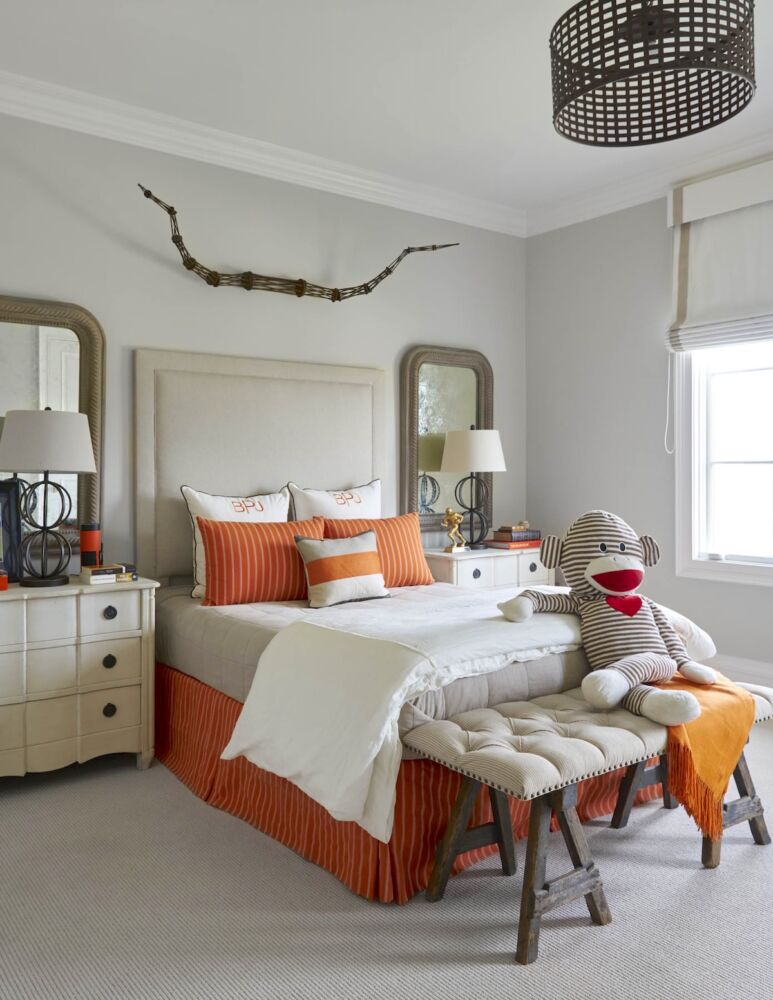 Child's bedroom with orange bedding, giant sock monkey on bench at foot of bed, metal lamps and pendant.
