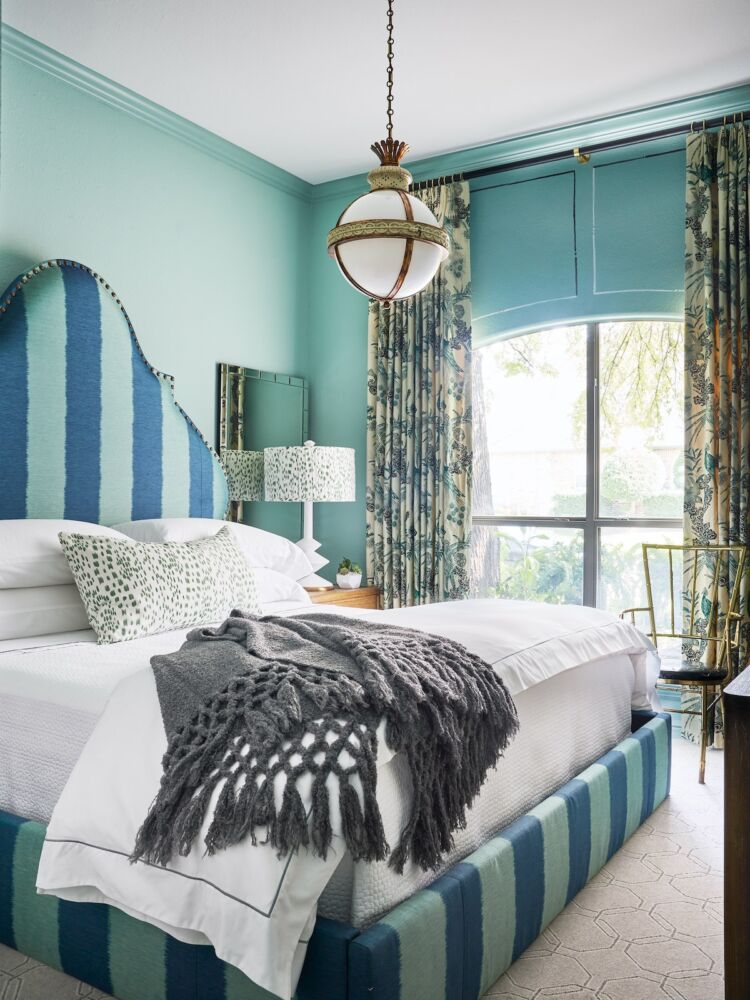 A guest room with a bold striped custom headboard, floral curtains and bedside lamps, topped with custom shades and a globe-style pendant lamp.