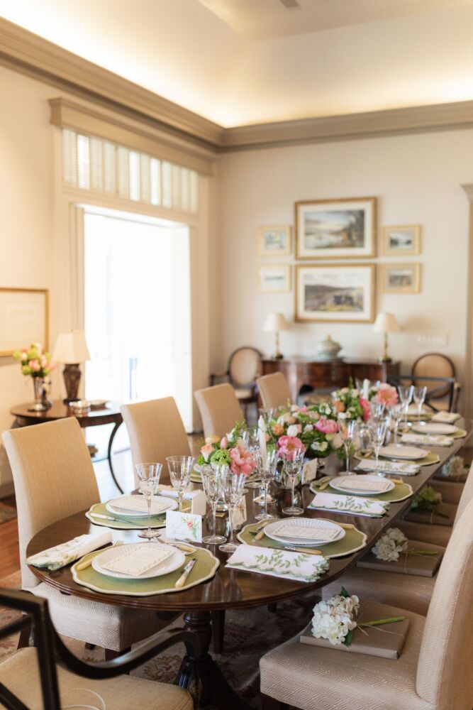A large table is filled with green and pink bouquets and personalized place settings.