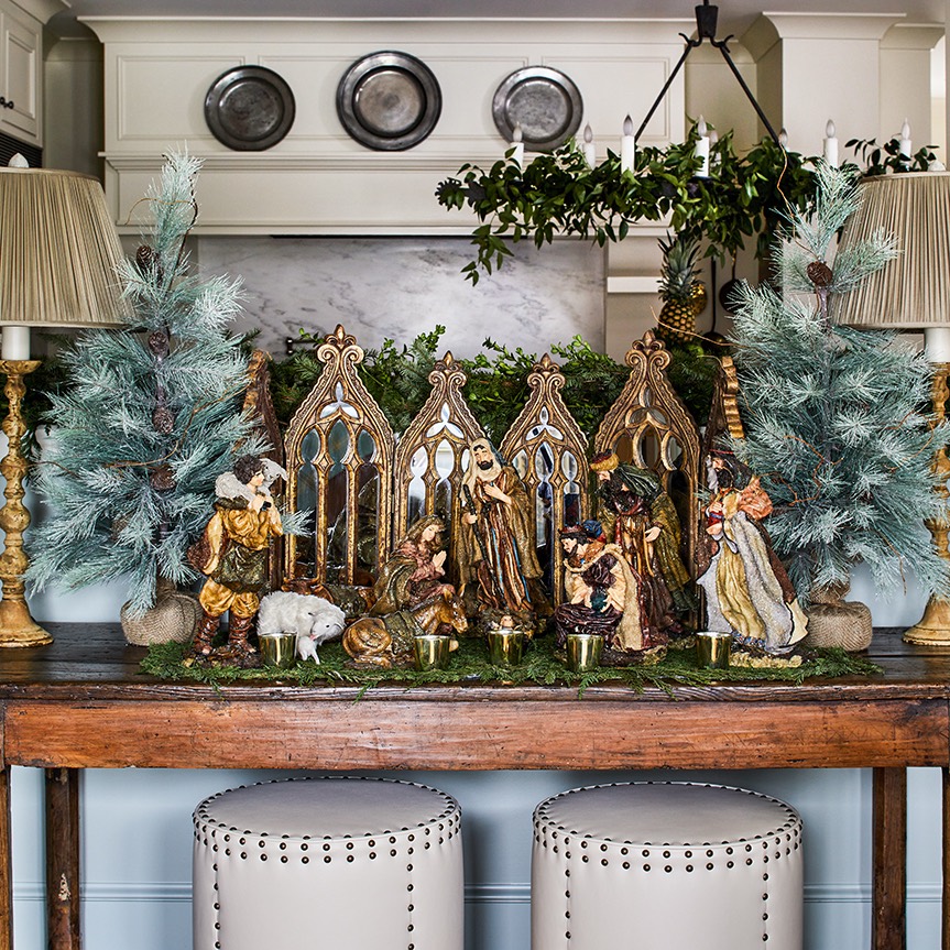 Nativity scene flanked by small blue-green Christmas trees on sideboard.