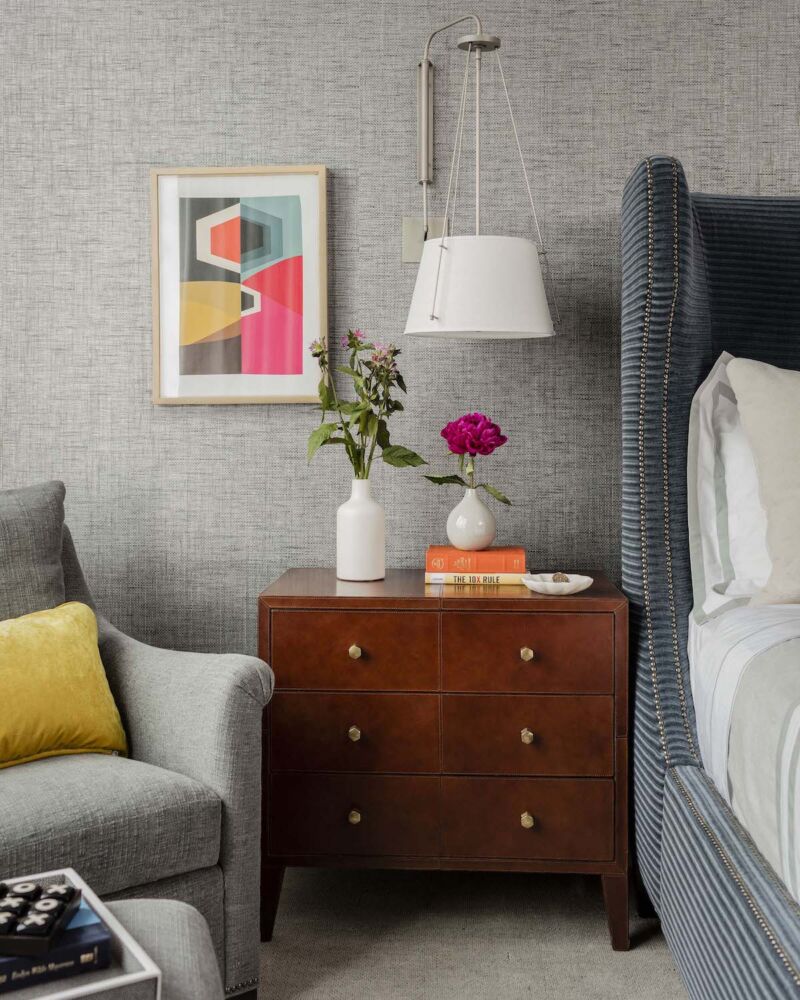 Boston area designer Robin Gannon hung contemporary sconces for bedside reading against a gray upholstered wall with jolts of color in the mix.