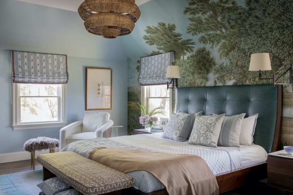 A leather headboard sits over scenic wallpaper along with a bold tired chandelier and swing arm lamps.