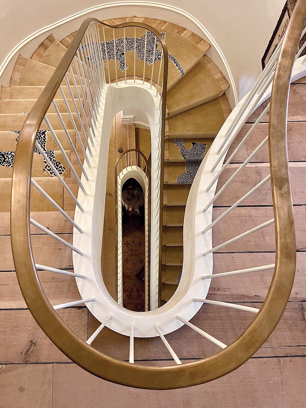 Three story stairwell with brass railing and climbing leopard runner, looking down from second story landing.