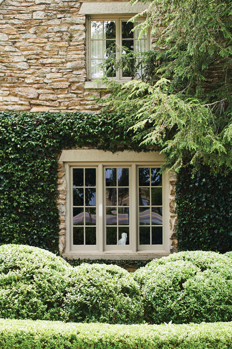 mullioned window surrounded by boxwoods, climbing vines, and overhanging branches