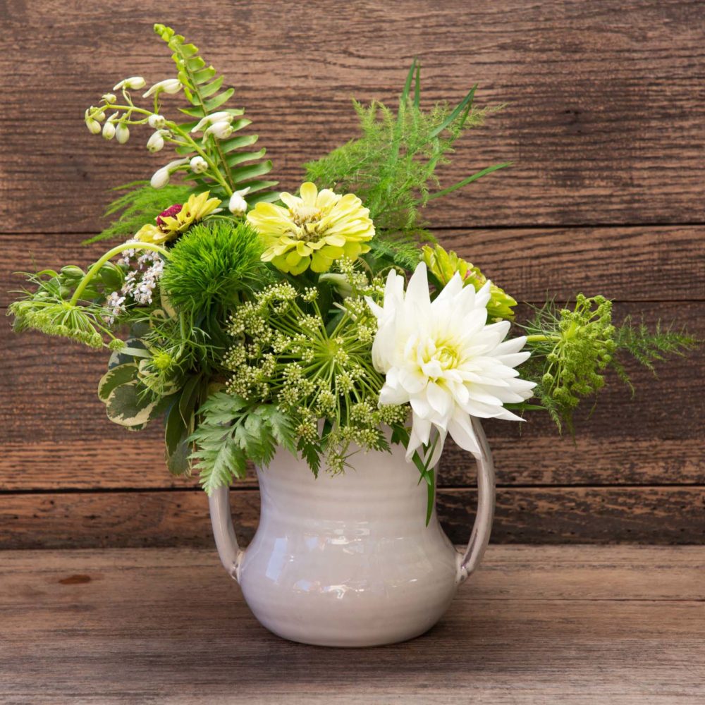 White ceramic jar with two handles, filled with green and white flowers.