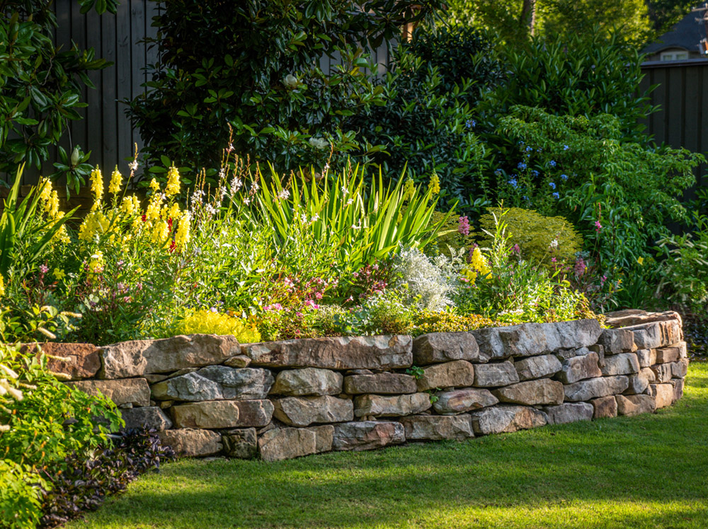 a raised stone bed planted with a variety of low and medium height plants, some in bloom