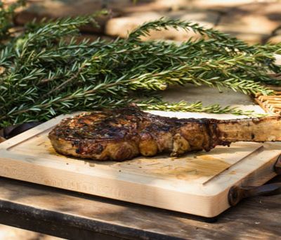 Seared bone-in rib-eye steak on a cutting board. A bundle of fresh rosemary lies beside it.