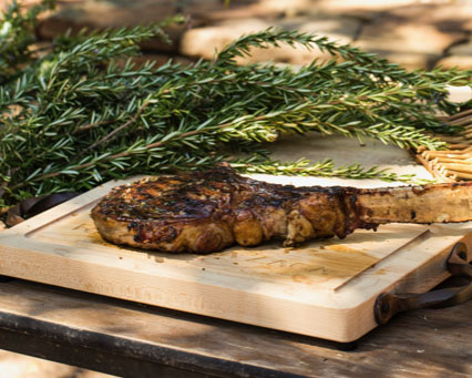 Seared bone-in rib-eye steak on a cutting board. A bundle of fresh rosemary lies beside it.