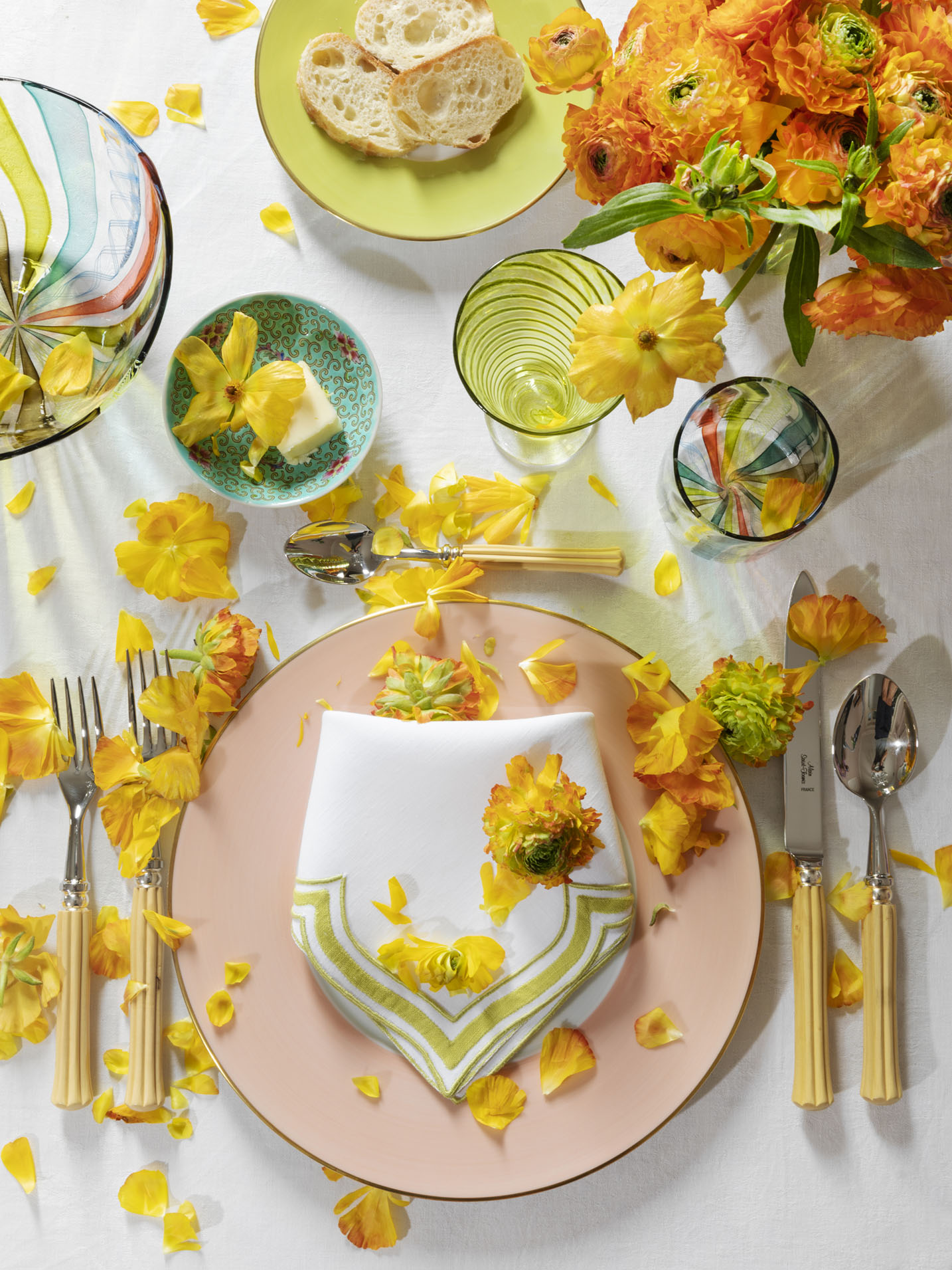 summer table from Rebecca Gardner's Houses & Parties featuring dinnerware in peach, green, and teal, with vibrant yellow and orange flowers