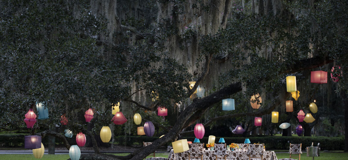 table set under a large old oak covered in Spanish moss. Colorful paper lanterns hanging in the tree set the scene aglow