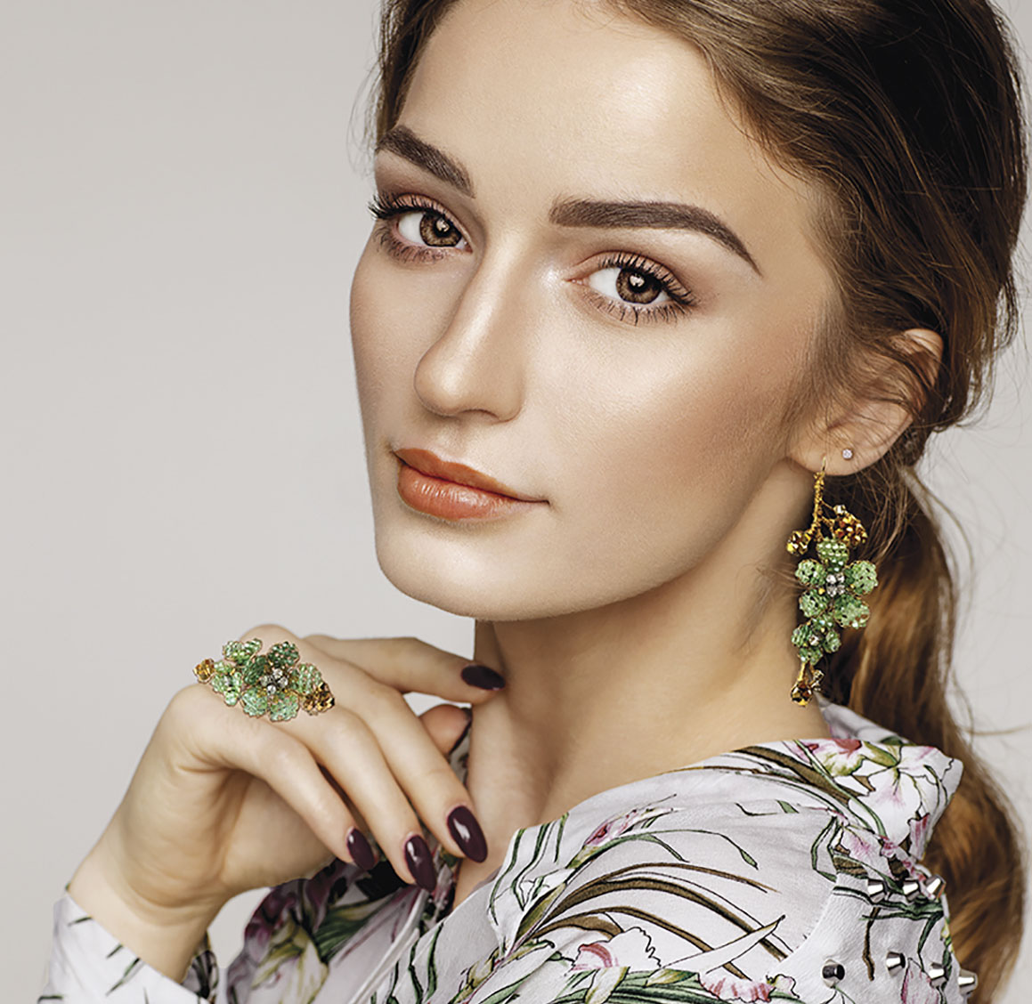 A model wearing a floral blouses poses with floral-inspired cocktail ring and earrings, both featuring green stones, by jewelry designer Mindy Lam