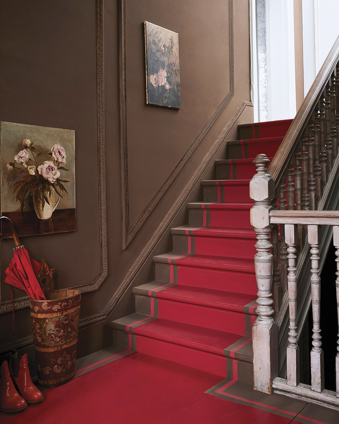 A stair case with walls and stairs painted brown with a red painted runner on the stairs and landing