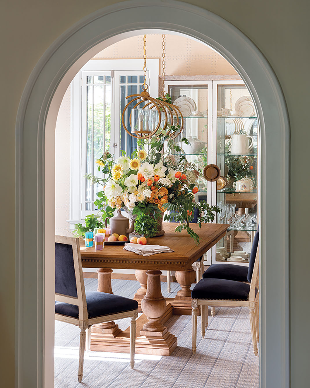 Framed by an arched entrance, a linear light fixture draws the eye through the dining room. The centerpiece features amaryllis, roses, ‘Italian White’ sunflowers, French tulips, wild grapevine, and wisteria. All floral designs by Jimmie Henslee. Interiors by Denise McGaha. Location: Dallas’ historic Highland Park