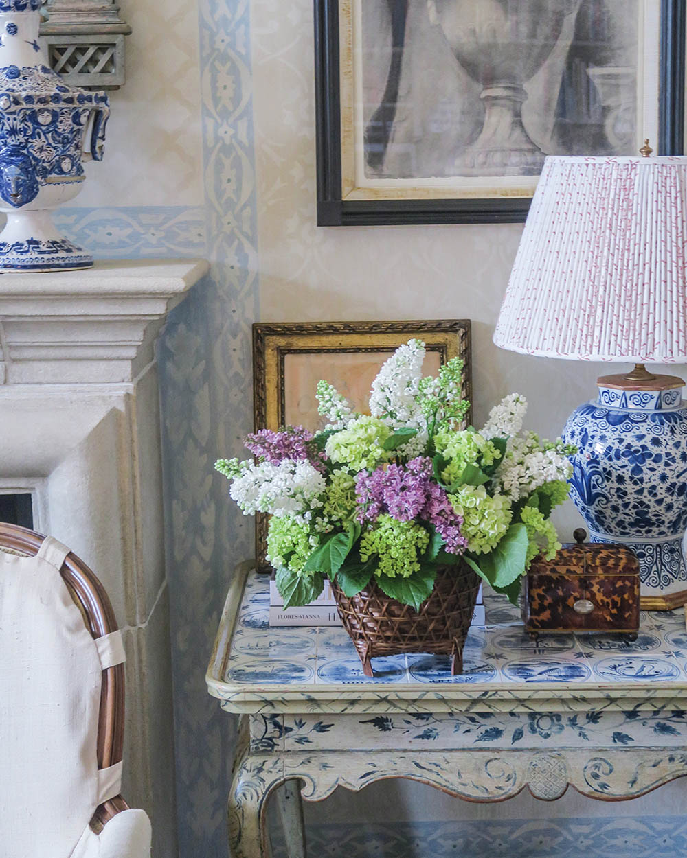 interiors vignette featuring a vase of lilacs on a side table beside a blue-and-white chinoiserie lamp