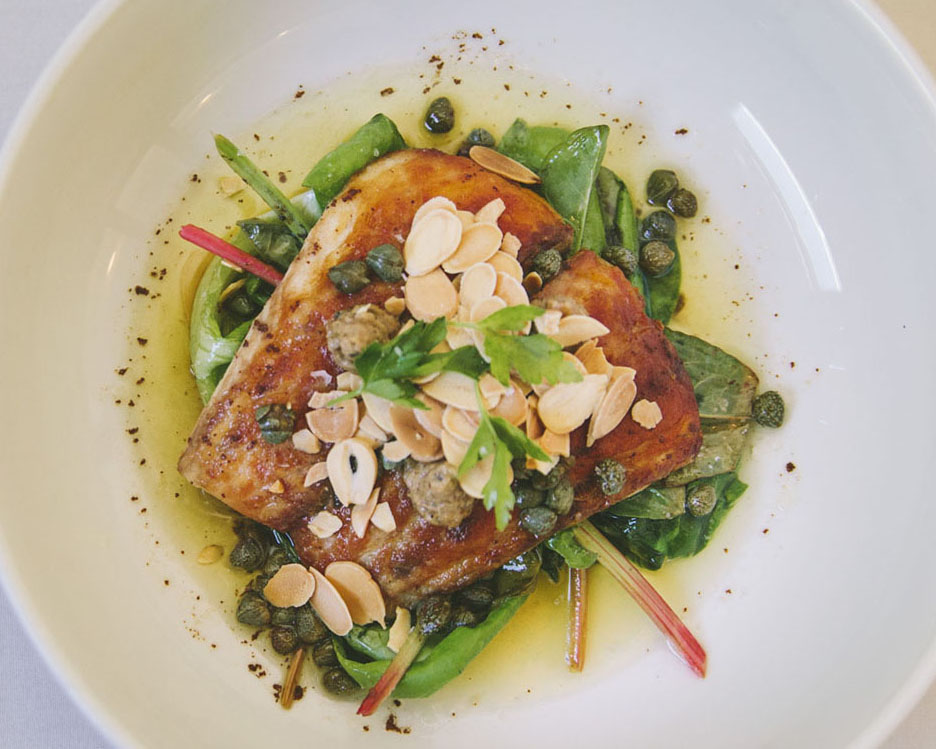 Elvie's Redfish Almondine, a pan fried fish dish topped with fresh herbs, charred lemon sauce, brown butter, capers, and sliced almonds