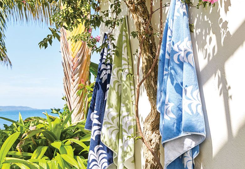 Beach scene with 3 towels in assorted colors from Heather Chadduck Hillegas’ collection for Weezie hung on a white stucco wal