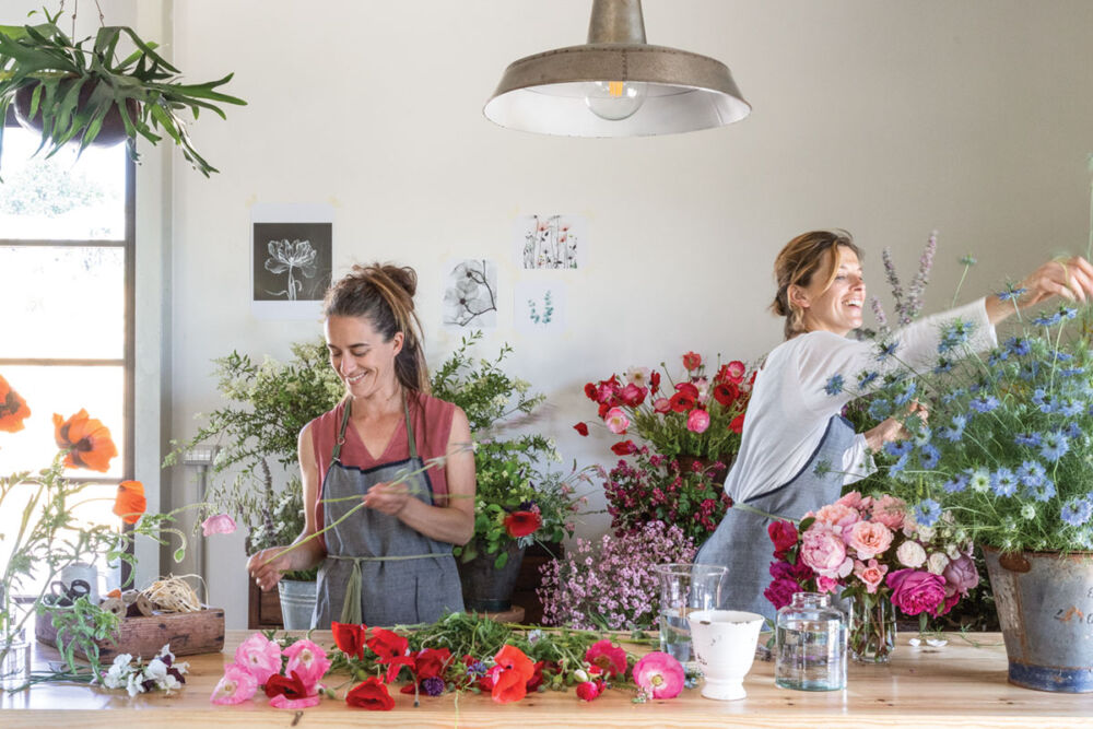 Teresa and Laura Cugusi, owners of PUSCINA FLOWERS, work at a long table filled with flowers.