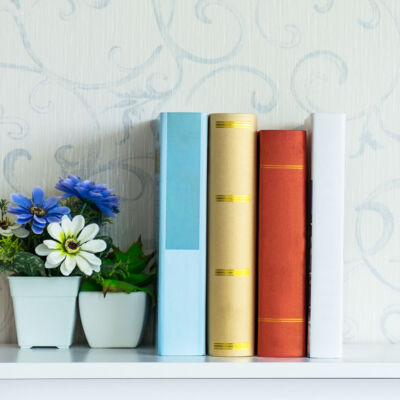 books lined up on a shelf beside a small vase of purple and white flowers