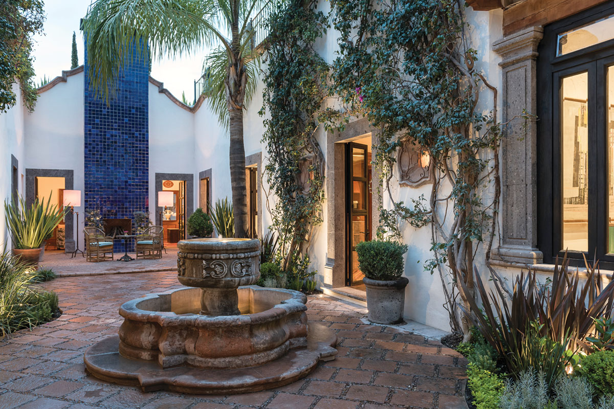 a fountain and terra cotta patio surrounded by white stucco one-style buildings and tropical plantings at Hotel Amparo