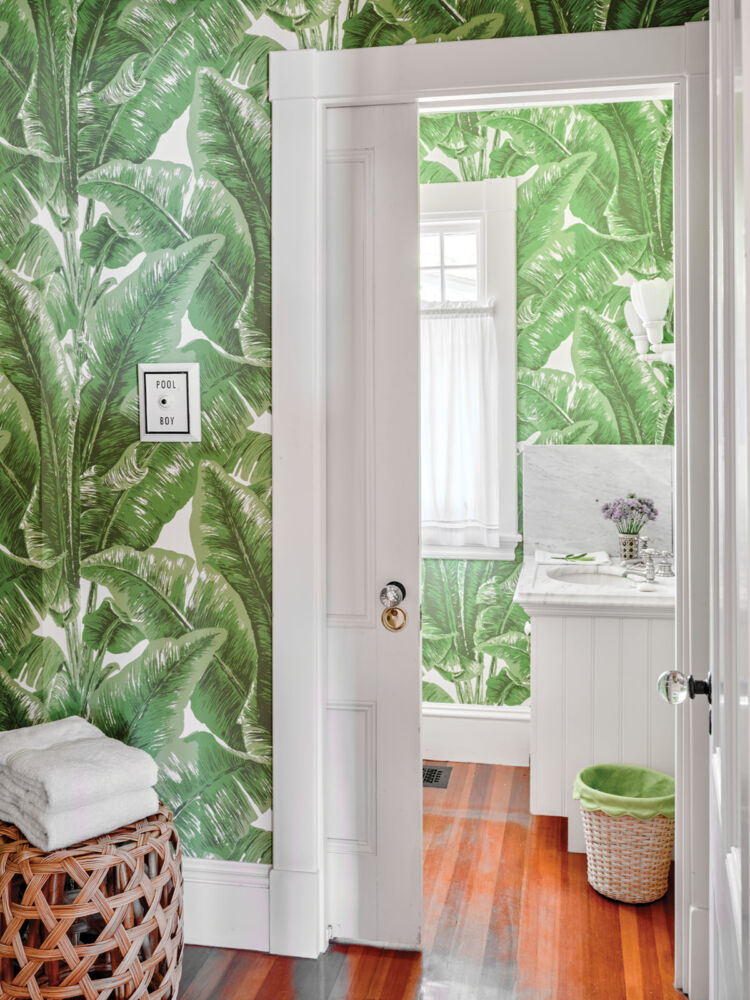 A wallpaper featuring of print of large green tropical leaves covers the powder room walls