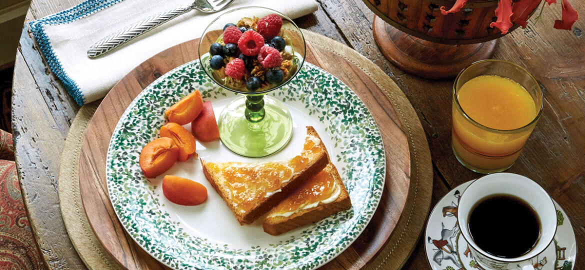 breakfast of toast, berries and granola, and sliced peaches set on a rustic wooden table