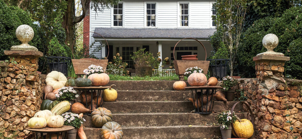 A display of pumpkins and other squash in cream, pale orange, and yellow decorate steps flanked by stone pillars. In the background is Keith Robinson's two-story white farmhouse