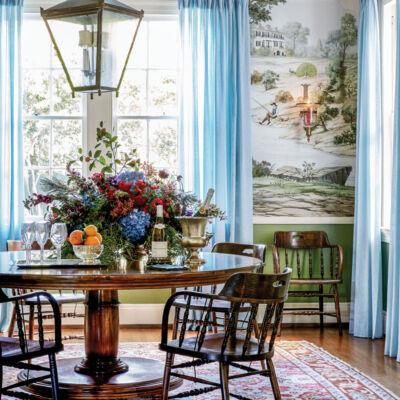 Dining room in the New Orleans home of Ware Porter. Features: Scenic wallpaper in a green colorway, pale blue sheer drapery panels, antique circular wood dining table and chairs, oriental rug, pale blue ceiling