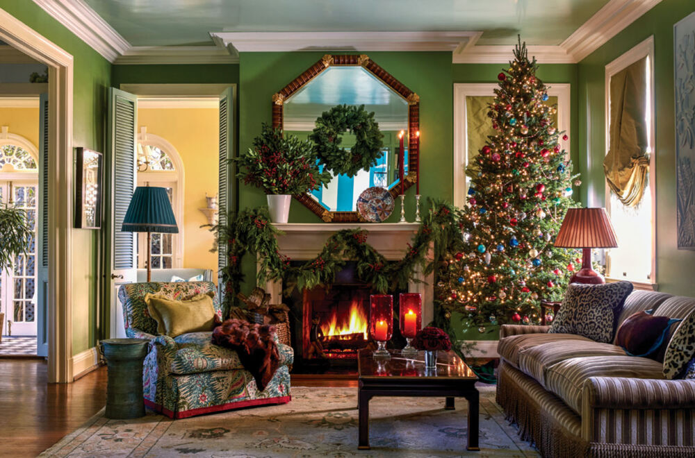 Sumptuous green living room in the New Orleans home of Ware Porter. Features: roaring fire, octagonal mirror above mantel, a tone-one-tone striped champagne-colored velvet sofa, large botanical-print armchair, decorated Christmas tree, mantel swags, wreath on mirror, and large arrangement of greenery and berries on the mantel