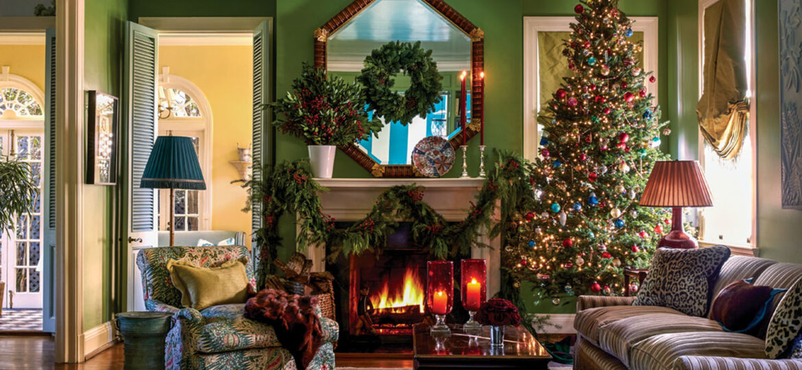 Sumptuous green living room in the New Orleans home of Ware Porter. Features: roaring fire, octagonal mirror above mantel, a tone-one-tone striped champagne-colored velvet sofa, large botanical-print armchair, decorated Christmas tree, mantel swags, wreath on mirror, and large arrangement of greenery and berries on the mantel