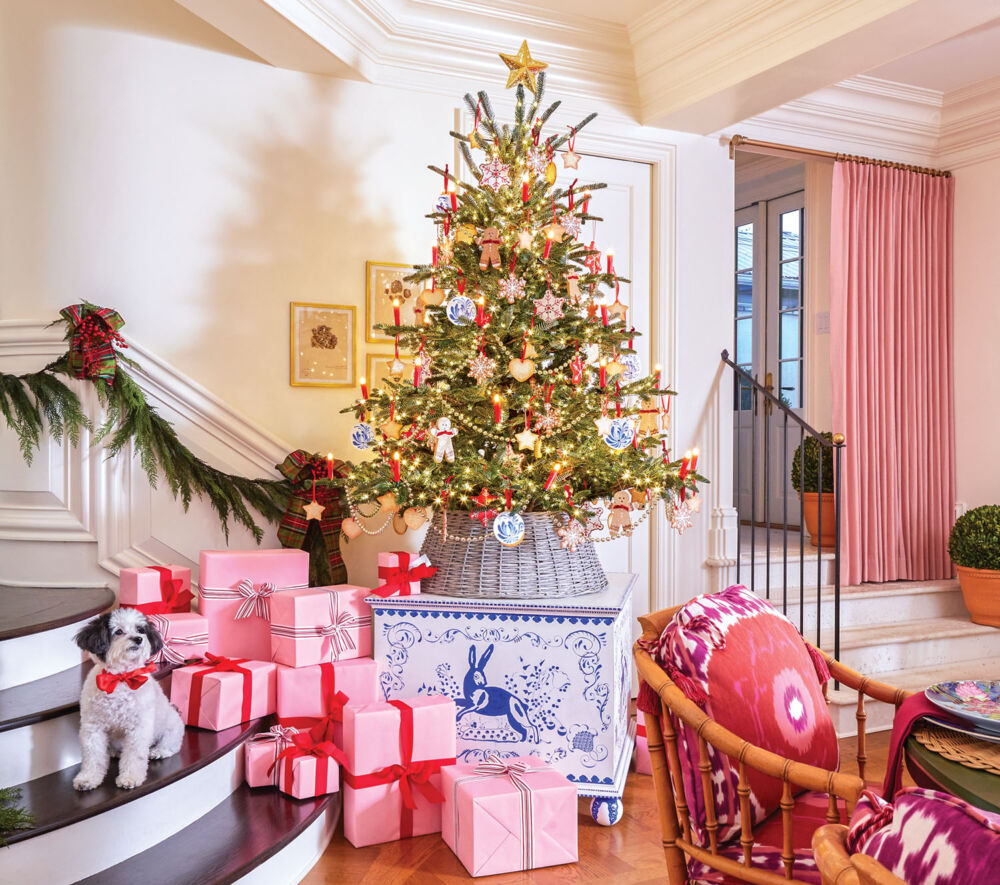 Christmas presents wrapped in pink paper and tied with red or silver ribbon are stacked on the stairs beside a tabletop tree set on a blue-and-white toy chest