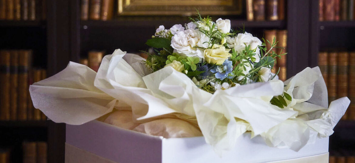 India Hicks's Wedding Party Flowers, bouquet set in tissue paper in a white box, with a moody English home library in the background