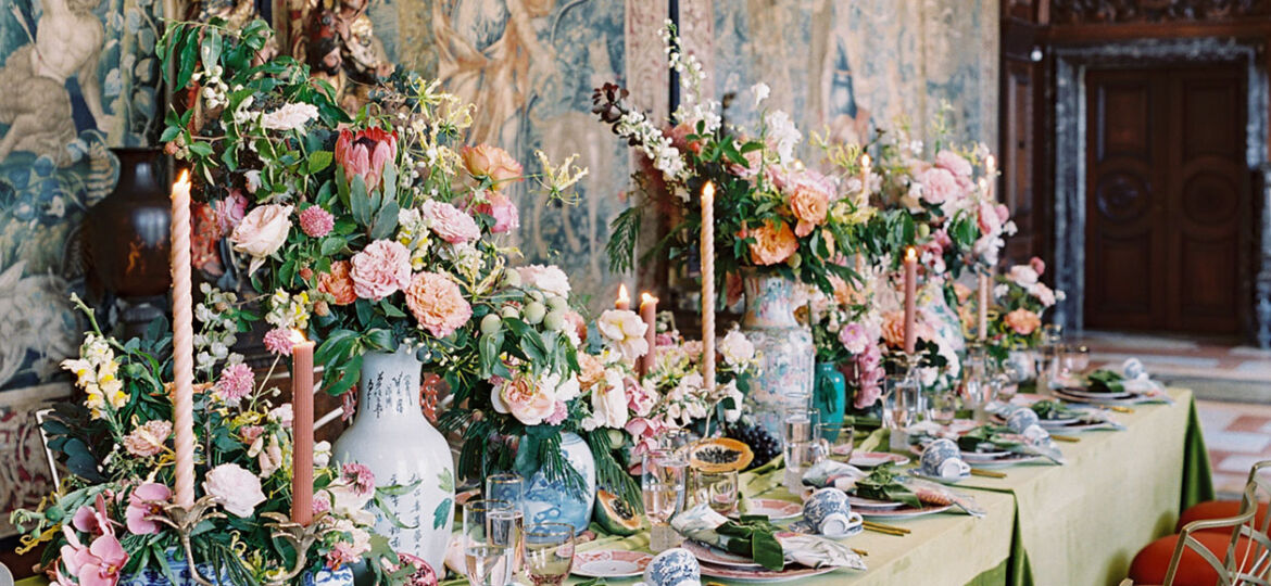 An opulent table filled with flowers and set on green velvet, set against the backdrop of Flemish tapestries at the Anderson House