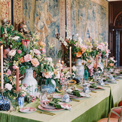 An opulent table filled with flowers and set on green velvet, set against the backdrop of Flemish tapestries at the Anderson House