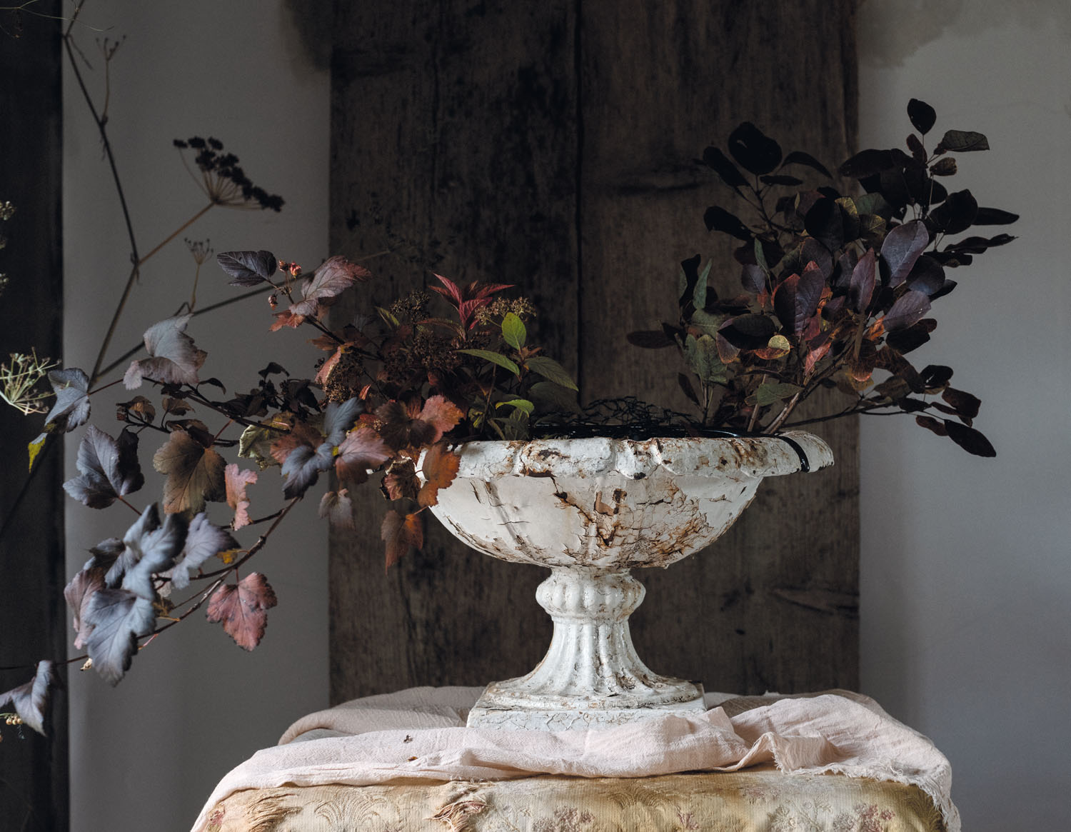 Branches of autumnal color ranging from deep purple to brown to red, establish an S-curve shape for The Flower Hunter Lucy Hunter's autumnal arrangement