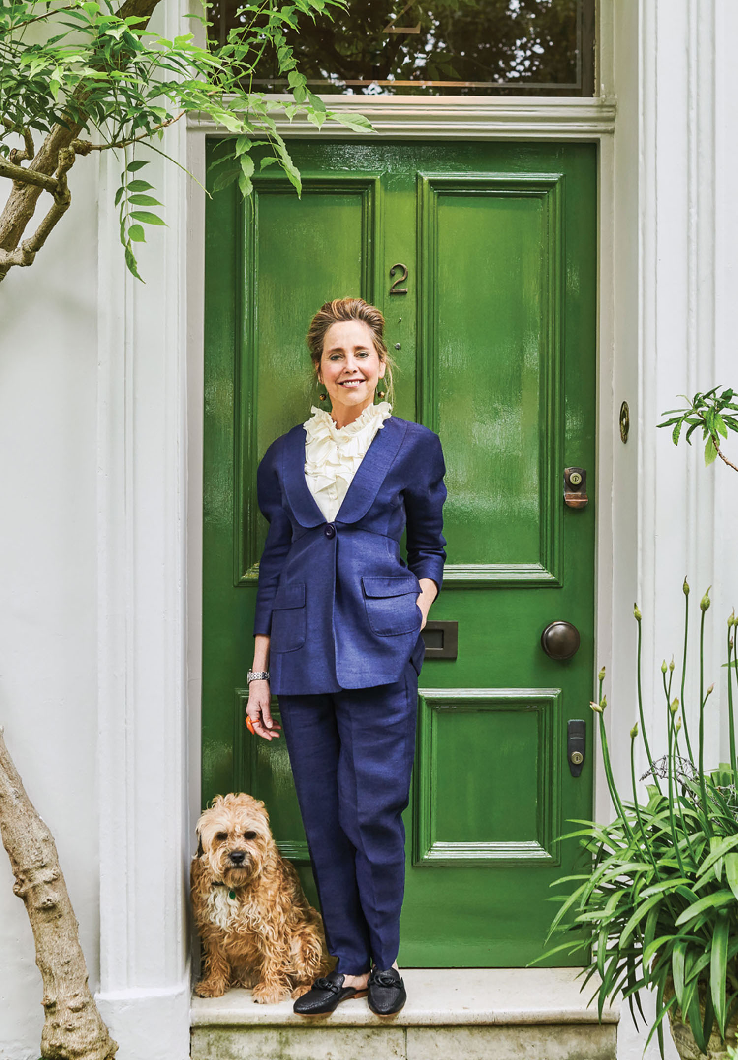 Portrait of garden designer Butter Wakefield in a navy pants suit standing in front a door painted glossy apple green