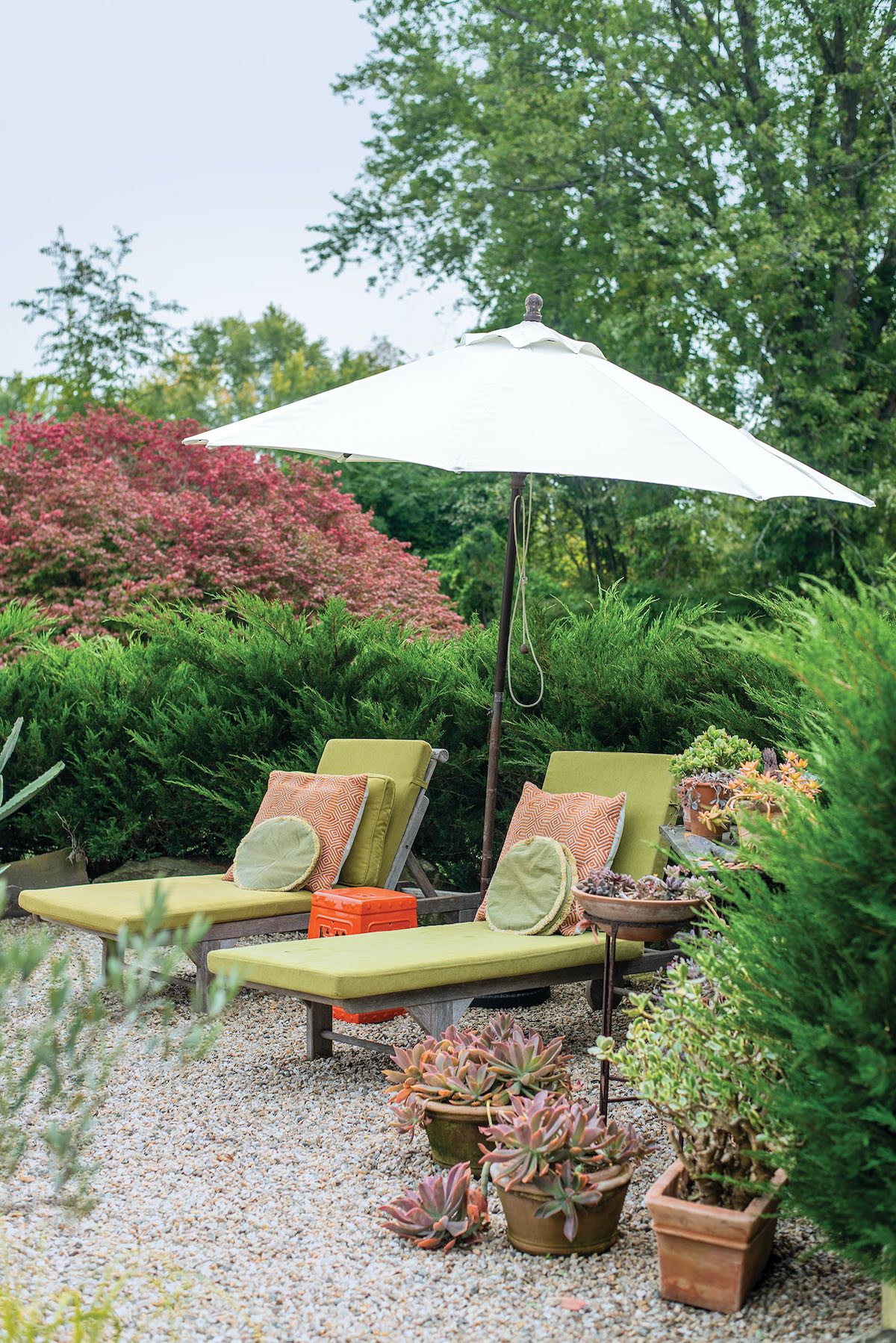 Lounge chairs under folding umbrella on gravel area in garden
