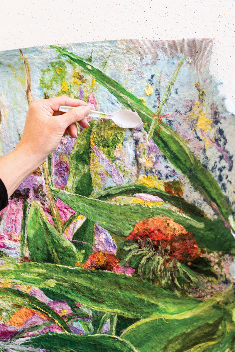 Artist Meg Black applying paint to canvas with a plastic spoon.