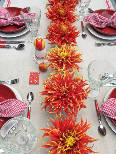 Centerpiece made of a line of single red and yellow dahlia blossoms down center of table.