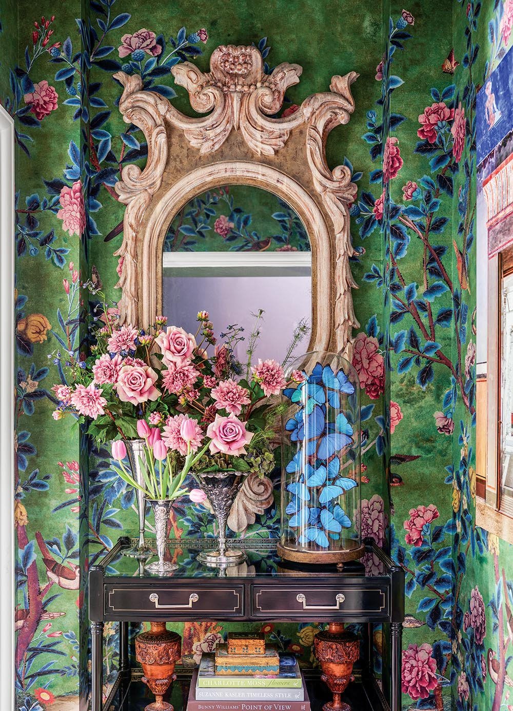 Bedroom vestibule with table topped with silver vases of pink roses and a cloche of blue butterflies.