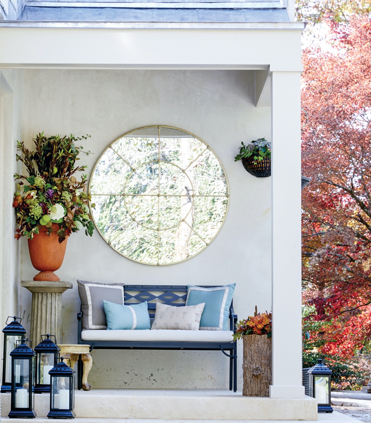 Back porch with bench, column pedestal with large flower arrangement, metal candle lanterns, and a large round mirror.