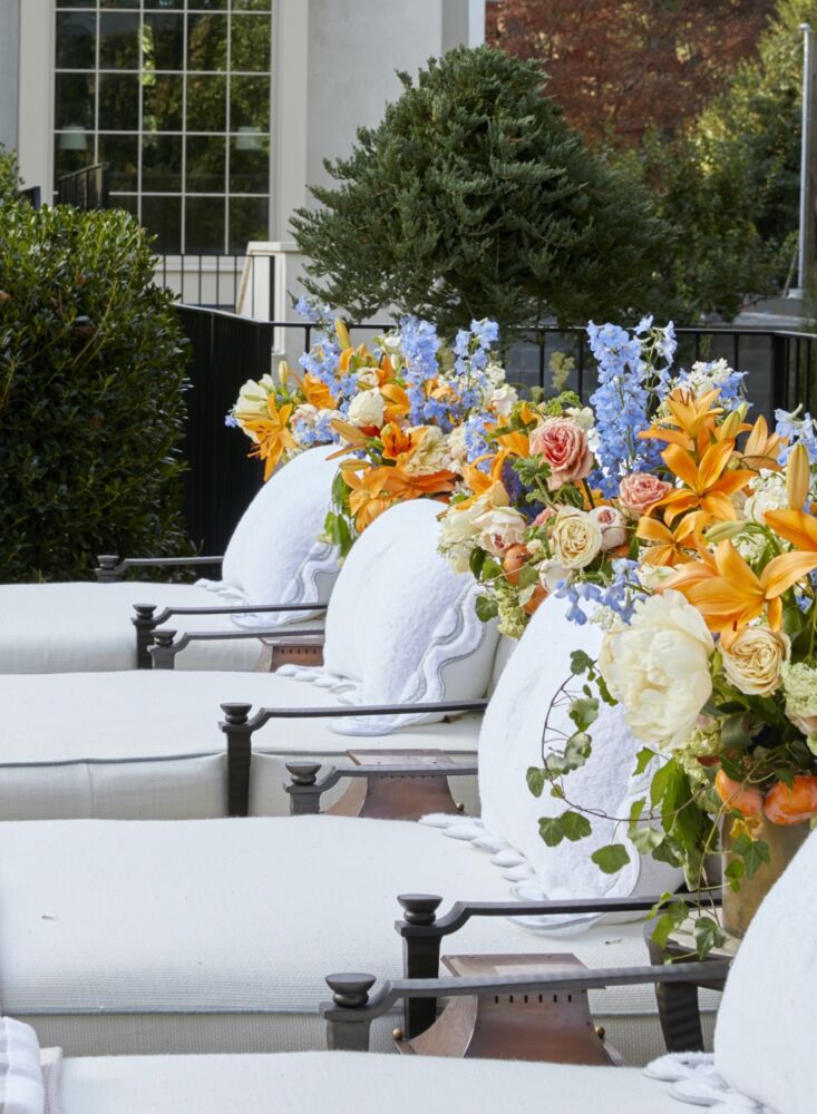 Line of poolside loungers with arrangements of tiger lilies, roses, peonies, and blue delphiniums.